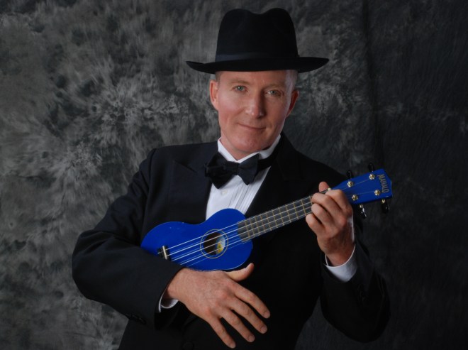 Will McMillan wearing a tuxedo and strumming a blue ukulele